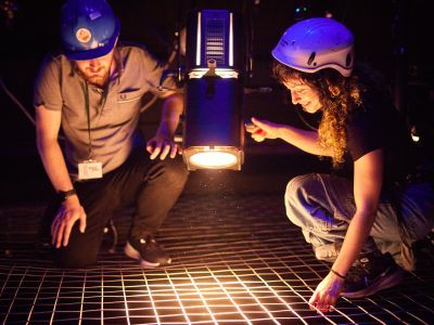 Image of two people wearing helmets using light above stage